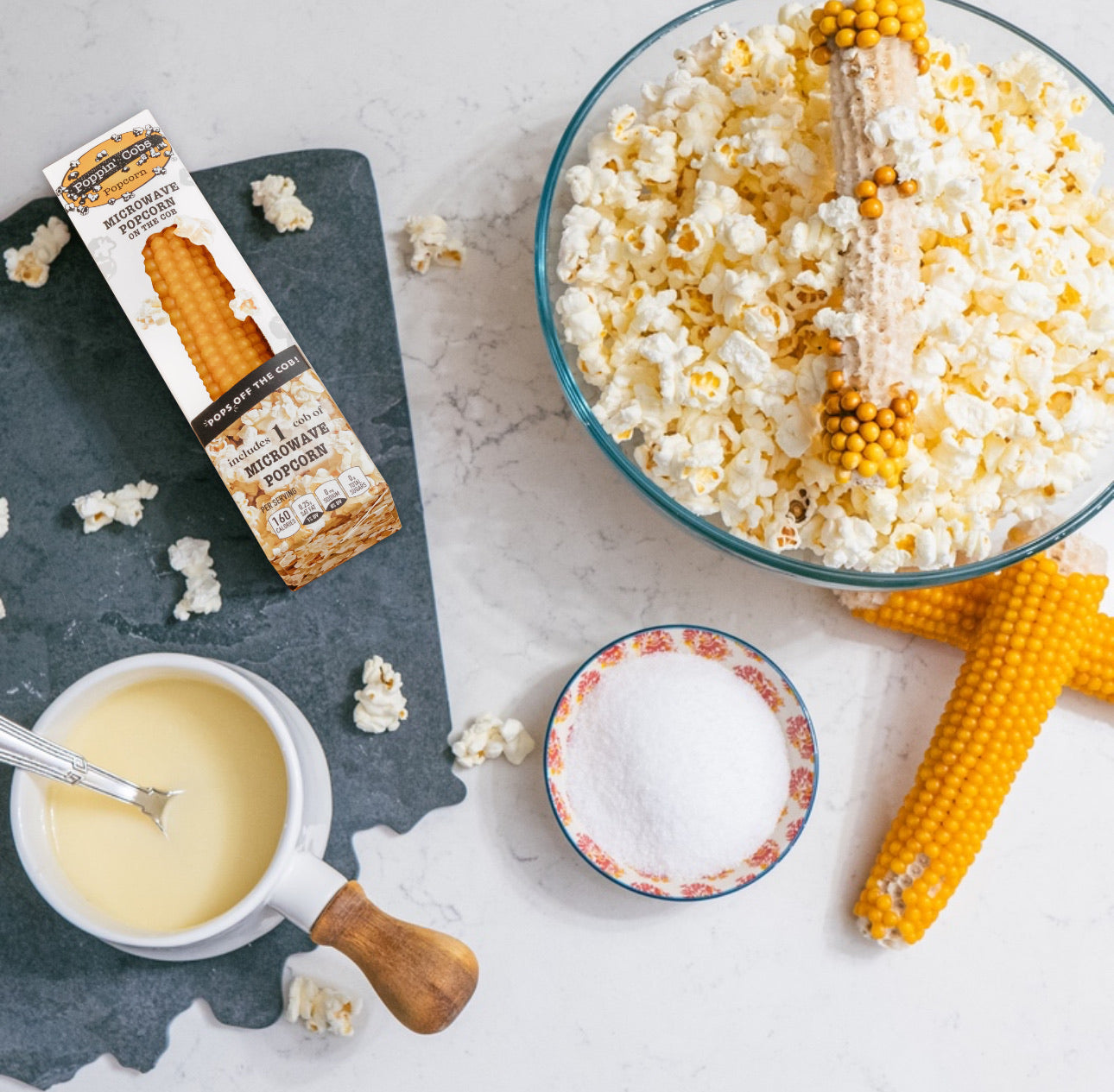 Popcorn-making setup with popcorn kernels, salt, and a bowl of popped popcorn on a light surface.